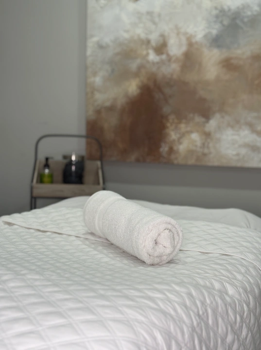 Massage table at Liv Aesthetics Med Spa in New Fairfield, CT, neatly prepared with a rolled white towel and quilted linens.